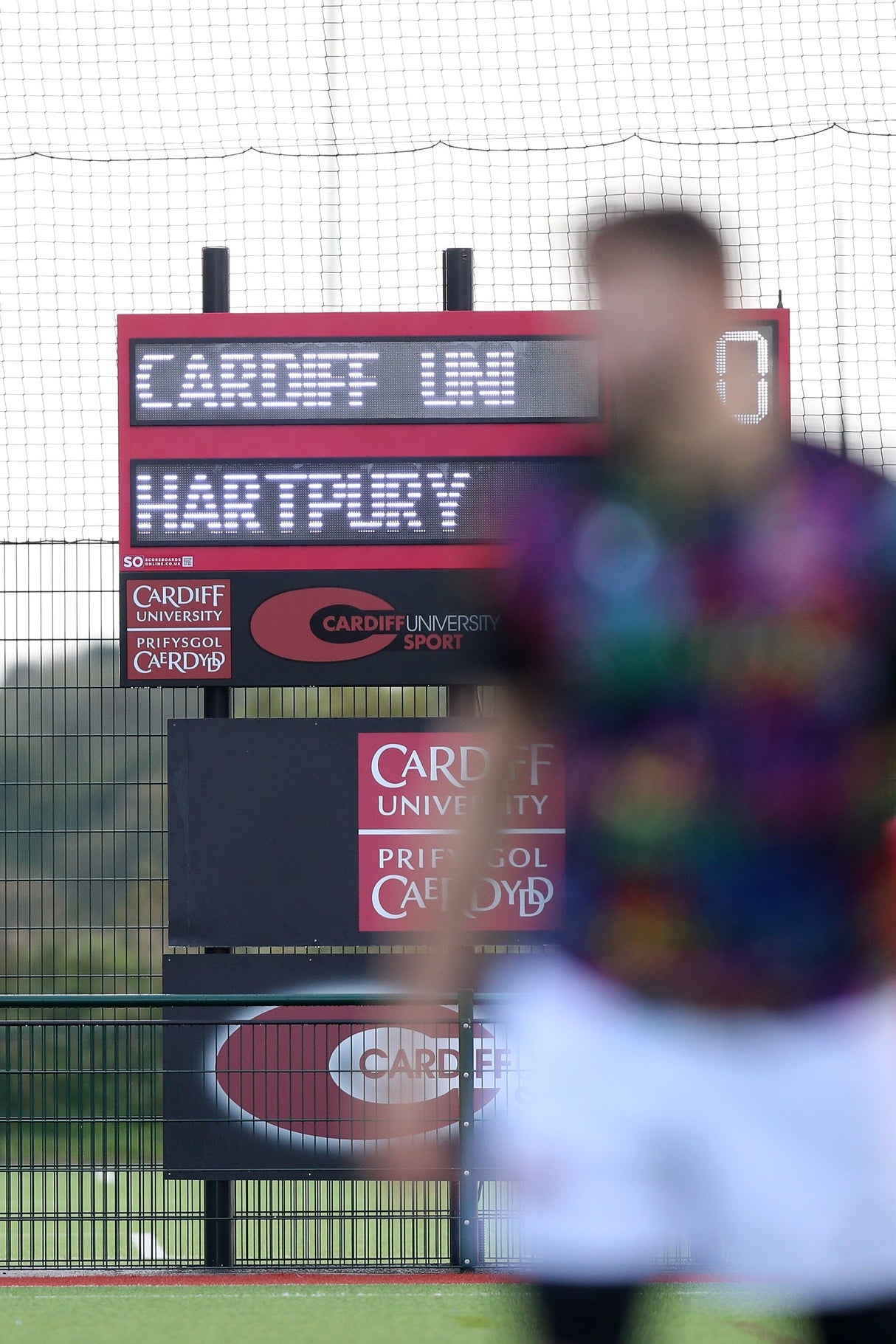 Scoreboard displaying 'Cardiff Uni' and 'Hartpury' with a blurred person in the foreground. Our ProXL Electronic Scoreboard with Editable Names