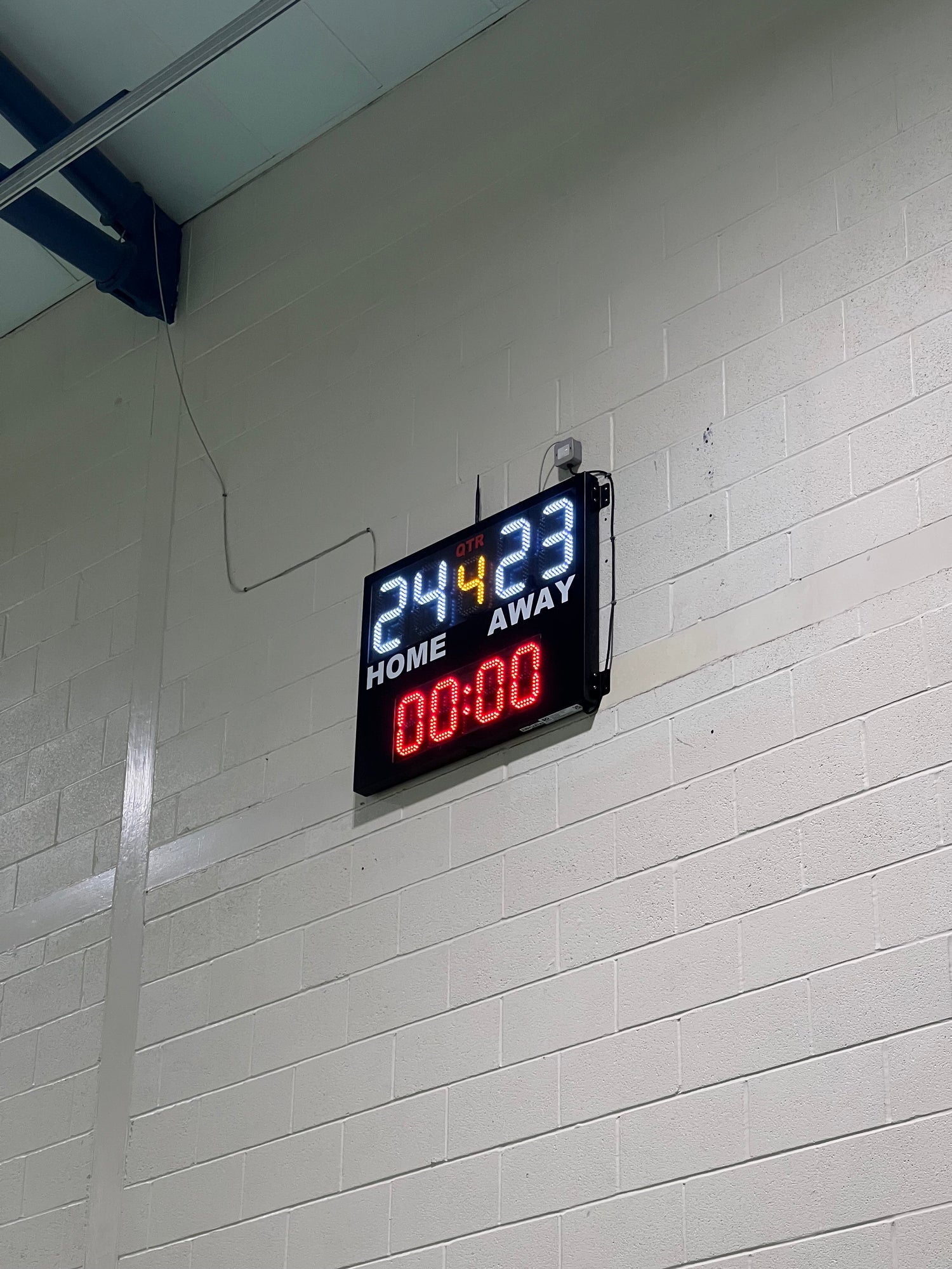 Digital LED electronic scoreboard on a sports hall wall with scores and time displayed