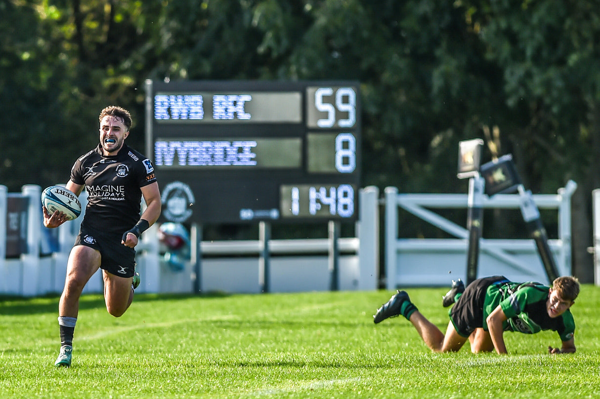 Rugby player running with the ball on a field with a scoreboard in the background