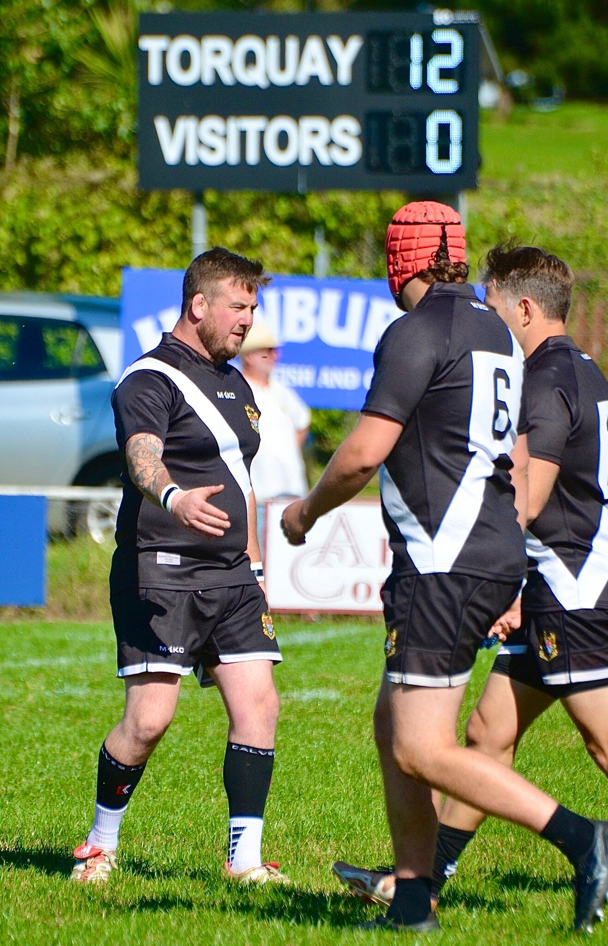 electronic rugby scoreboard behind players on a rugby pitch